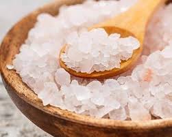 A wooden bowl and spoon filled with pinkish-white rock salt crystals.